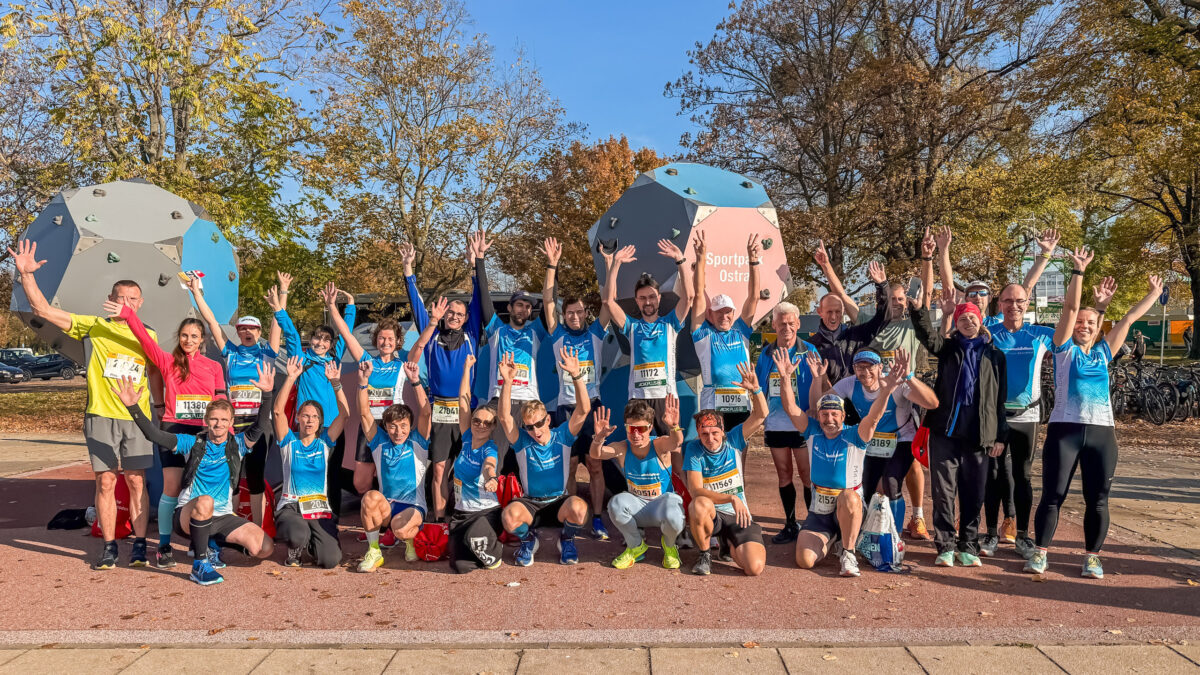 Die Laufgruppe Dresden trifft sich vor dem Start des Dresden Marathons im Sportpark Ostra für ein Gruppenfoto und alle strecken die Arme zum Himmel.