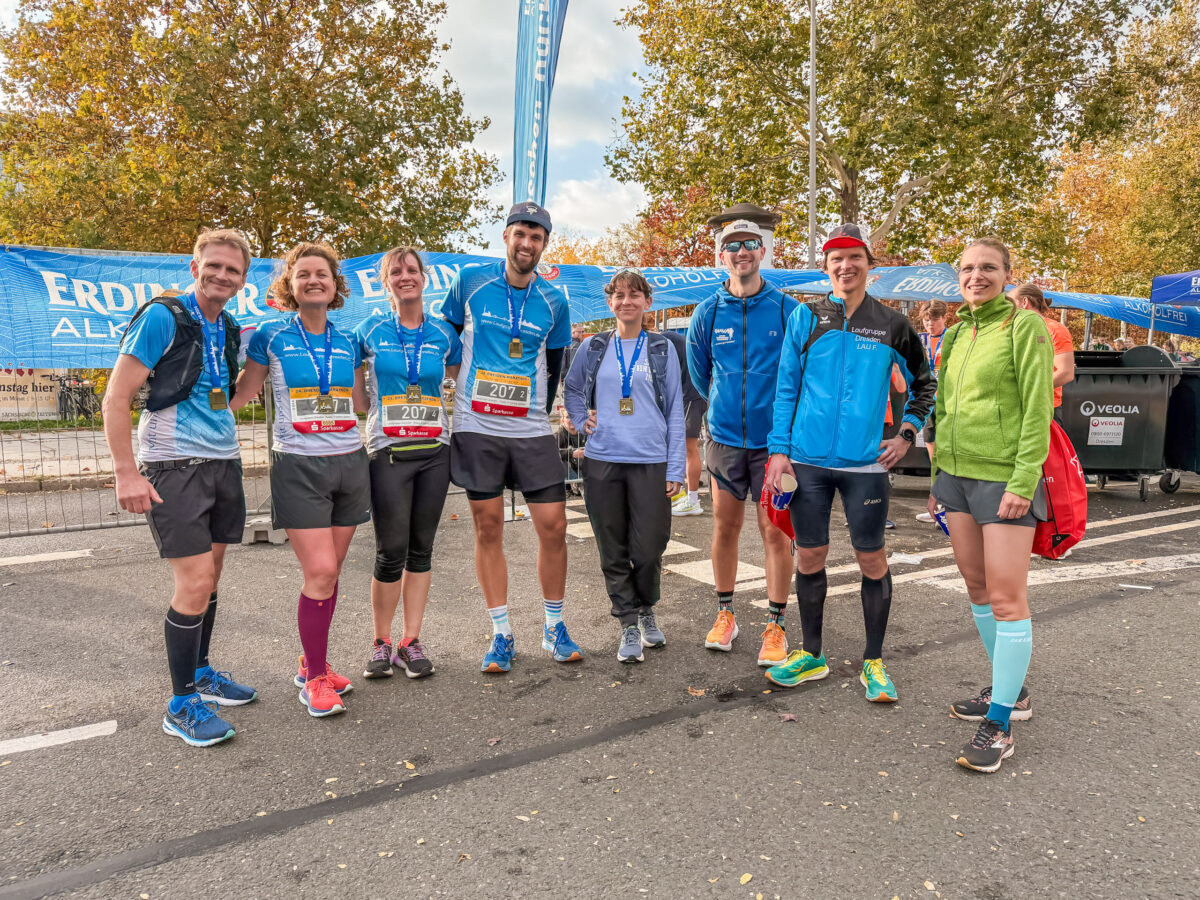 Zwei Staffeln der Laufgruppe Dresden stehen mit Medaillen behängt nach dem Zieleinlauf im Zielbereich des Dresden Marathons.